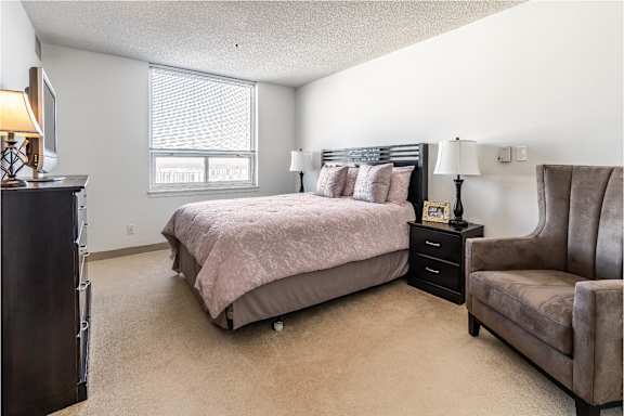 A bedroom with a bed, chair, and window.