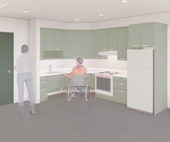 A person in a wheelchair is in a kitchen with green cabinets.
