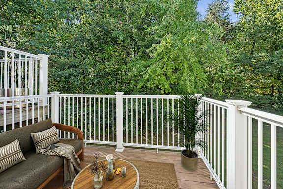 A white railing encloses a cozy balcony with a couch, table, and potted plant.