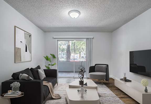 A living room with a grey couch, a white coffee table, and a flat screen TV mounted on the wall.