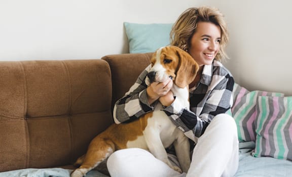A woman is sitting on a bed with a dog.