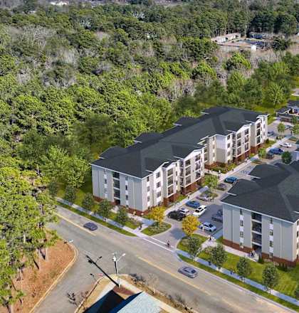A large apartment complex is surrounded by trees and is located near a road.