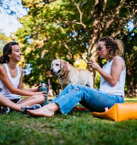 two women sitting on the grass with a dog