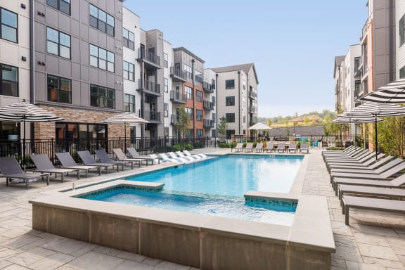 a swimming pool with chairs and umbrellas in front of an apartment building