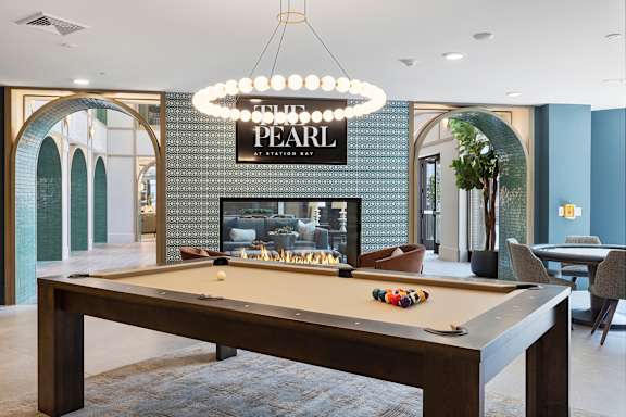 A pool table with a lighted sign that says "PEARL" above it.