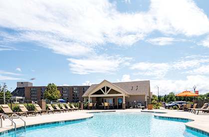 A swimming pool surrounded by lounge chairs and umbrellas with a building in the background.