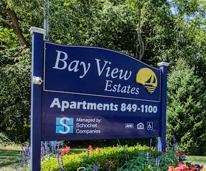 a sign for bay view estates apartments with flowers and trees