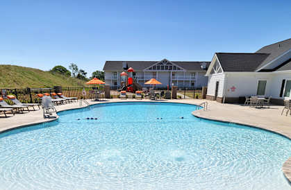 A pool surrounded by lounge chairs and umbrellas with a sign advertising a special offer for bedroom apartments.