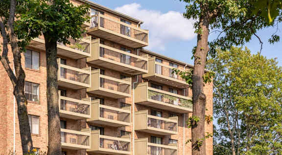 A tall apartment building with balconies and trees in the foreground.