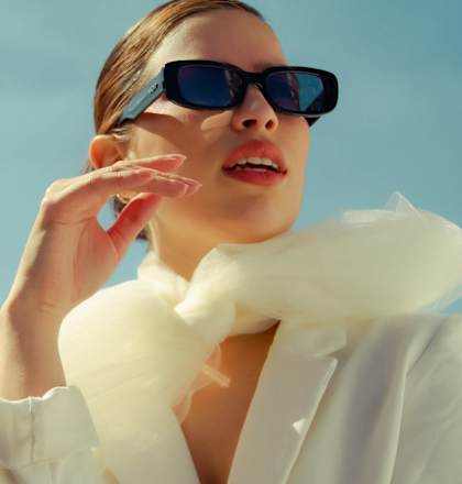 A woman wearing sunglasses and a white coat with a white scarf.