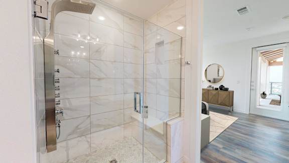 the master bathroom has a large shower with marble tiles and a wood floor