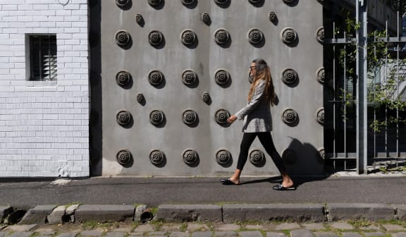 a woman walking down the street in front of a wall