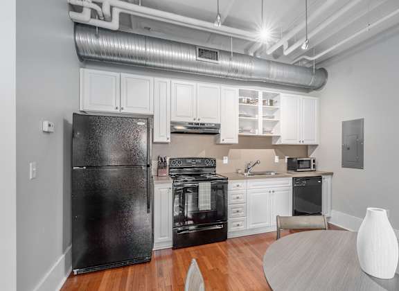 A black refrigerator is in a white kitchen with wooden floors.