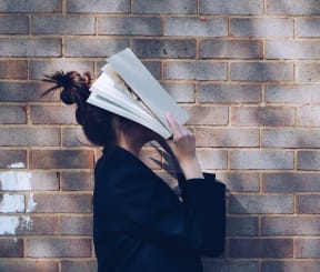 a woman standing in front of a brick wall with a book on her head