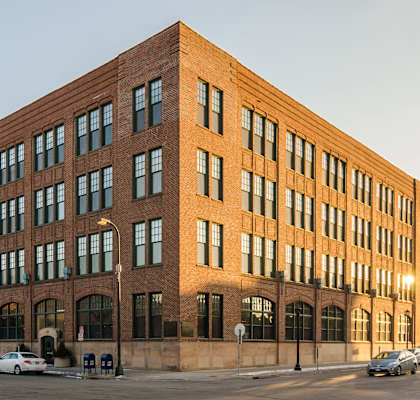 A large red brick building with many windows and cars parked in front.