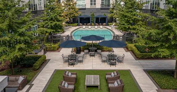an outdoor lounge area with tables and chairs and a pool in front of an apartment building