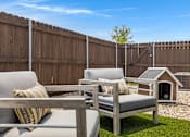 Thumbnail 4 of 8 - A backyard with a wooden fence and a grey couch with a striped pillow.