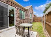 Thumbnail 3 of 6 - A patio with a table and chairs is set up outside a brick house.