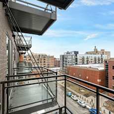 A balcony with a metal railing overlooks a parking lot and buildings.