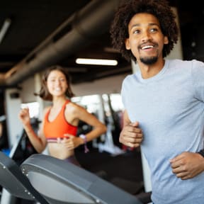smiling man running on a treadmill with a woman in the background