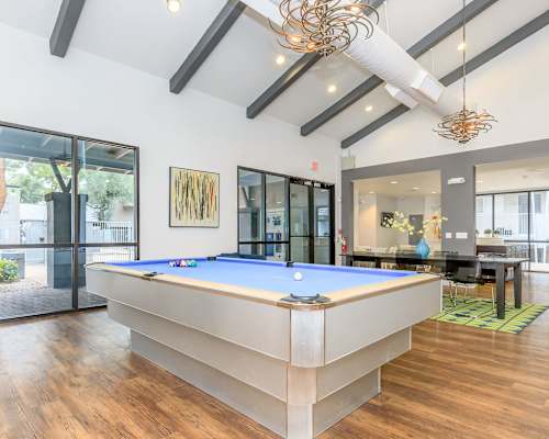 A pool table is in the middle of a room with wood floors and a ceiling with exposed beams.