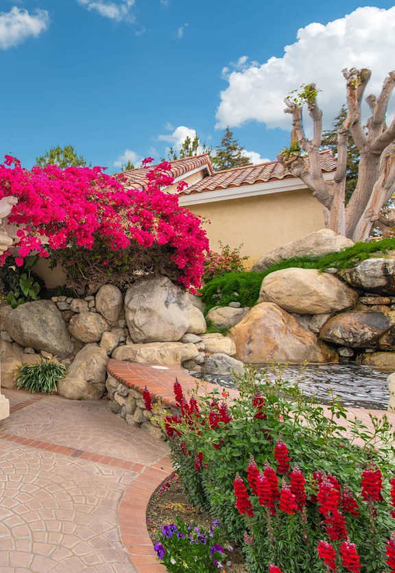 a patio in front of a house with pink flowers at Victoria Springs Apartments, Riverside, CA