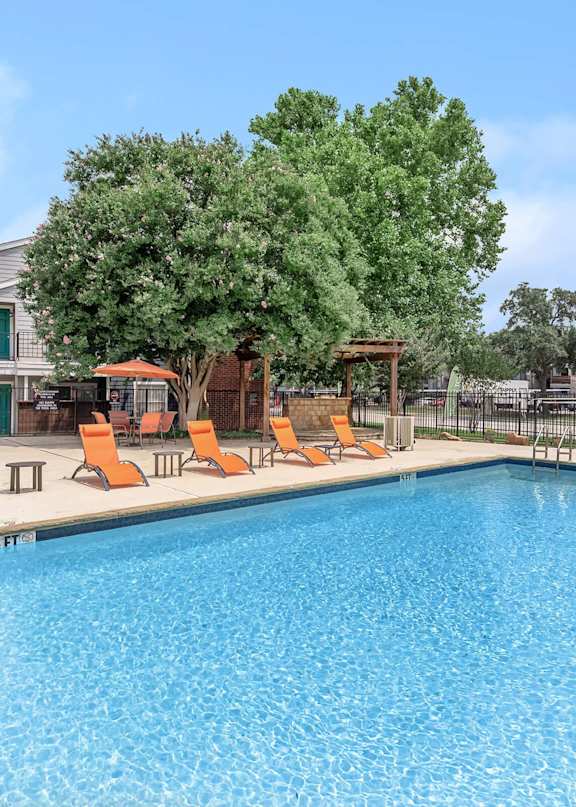 A swimming pool with orange lounge chairs and a tree in the background.