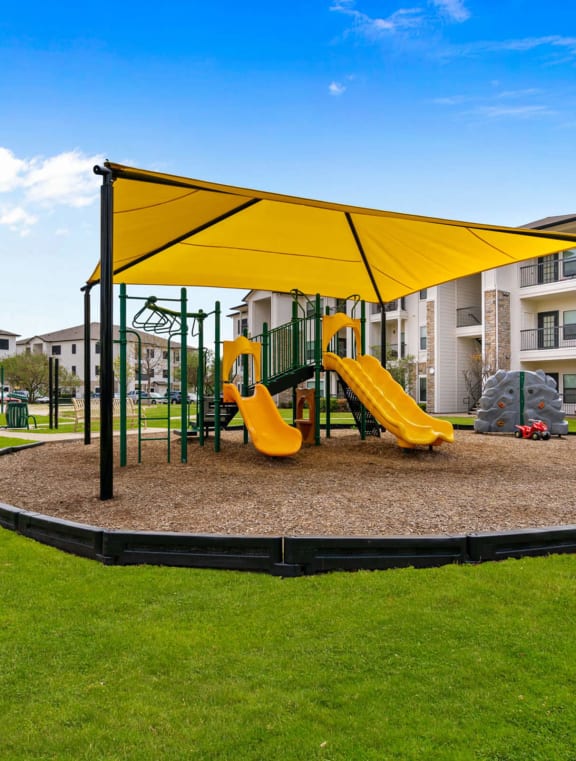 a courtyard with a playground and yellow chairs in front of an apartment building