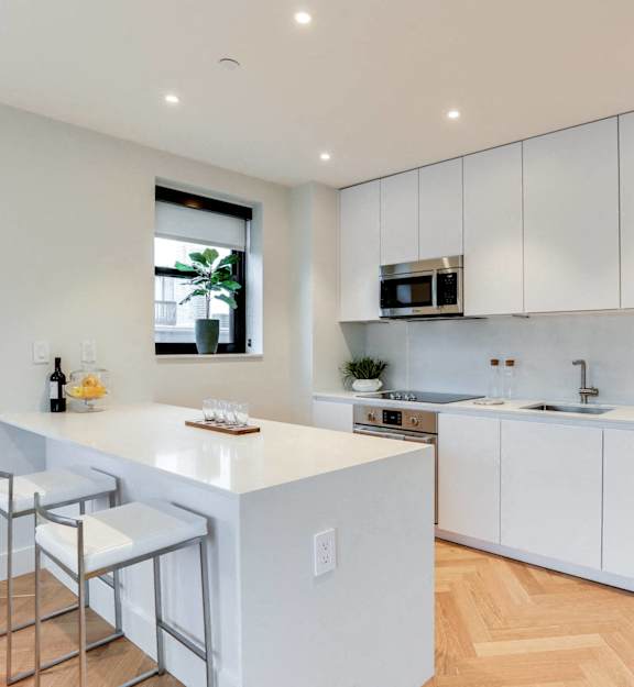 A modern kitchen with white cabinets and a wooden floor.