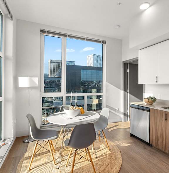 A modern kitchen with a table and chairs by a window overlooking a cityscape.