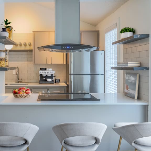 Kitchen with white cabinets and a white counter top with three white chairs in front of it