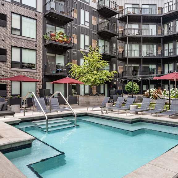 A large outdoor pool surrounded by lounge chairs and umbrellas.