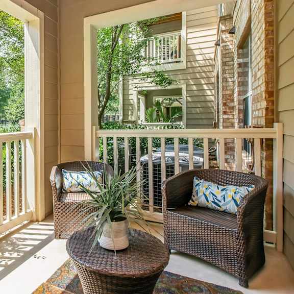 A balcony with a wicker chair and table with a potted plant on it.