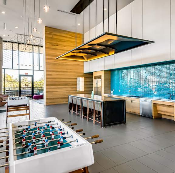 A foosball table is in the middle of a room with a kitchen area.