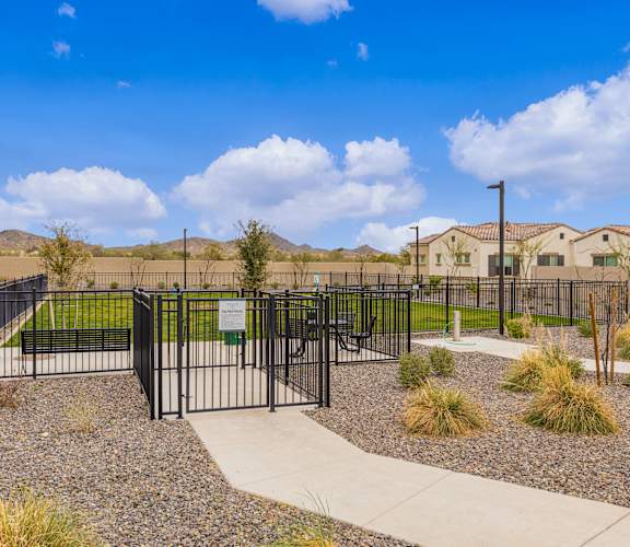 A black fence surrounds a gravel area with a concrete walkway and a green sign in the middle  at Avilla Canyon, Phoenix
