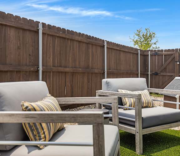 A backyard with a wooden fence and a grey couch with a striped pillow.
