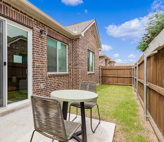 A patio with a table and chairs is set up outside a brick house.