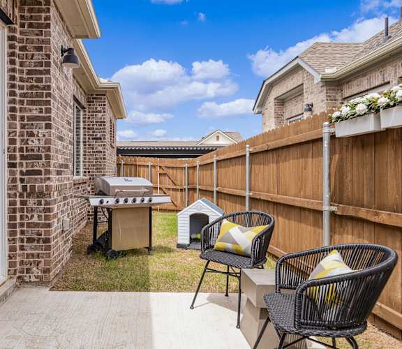 A backyard with a grill and two chairs.