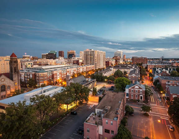 A cityscape at dusk with buildings and streets illuminated by streetlights.