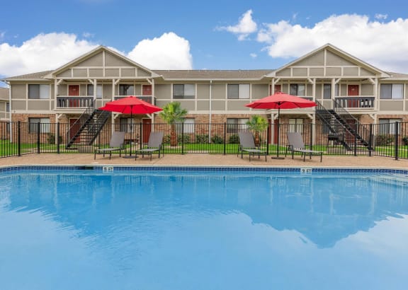 a large swimming pool in front of a building with umbrellas at Castlewood Apartments, Clute, TX, 77531