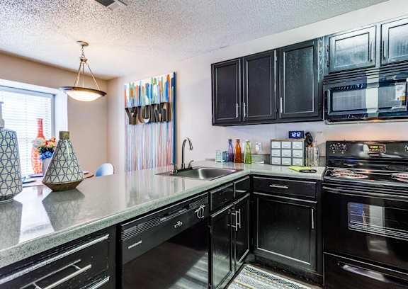A kitchen with black appliances and a grey countertop.