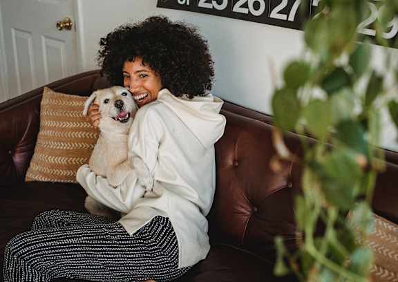 A woman with curly hair is sitting on a brown leather couch holding a white dog.
