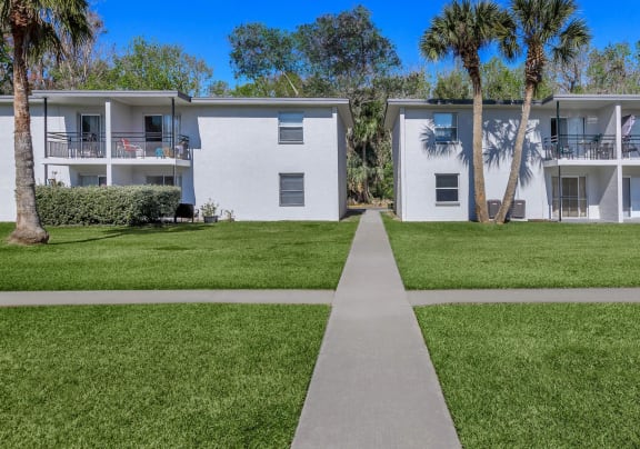a sidewalk in front of a building with palm trees at Palm Cove Apartments, Daytona Beach, FL 32114