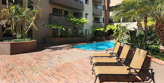 A pool surrounded by chairs and plants in front of a building.