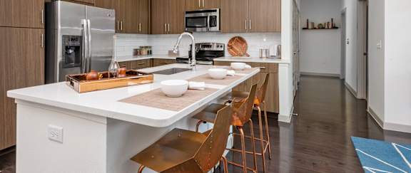 A modern kitchen with a white island and wooden chairs.