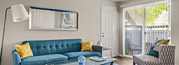 A living room with a blue couch and a glass table.