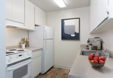 a kitchen with white appliances and a bowl of fruit on the counter