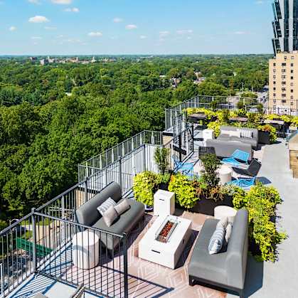 A rooftop patio with a table and chairs overlooks a cityscape.