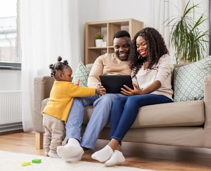 A family of three is sitting on a couch with a tablet in their hands.