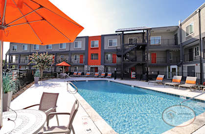 a swimming pool with an orange umbrella in front of an apartment building